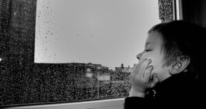 不満げに窓の外の雨を見つめる少年の横顔